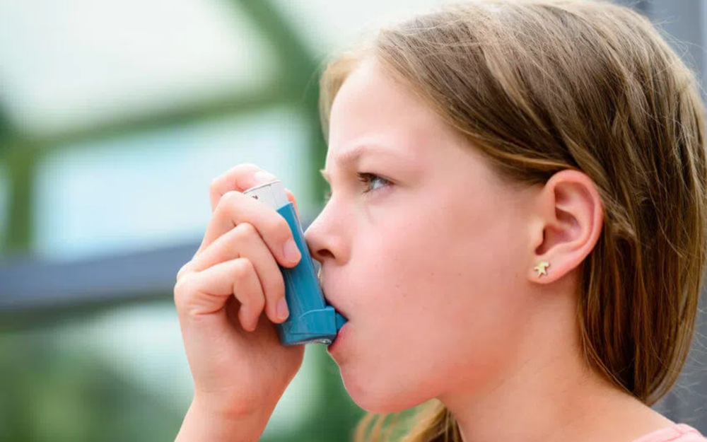 Dziecko trzymające inhalator i wykonujące inhalację leku wziewnego, widoczna dłoń z urządzeniem medycznym przy ustach