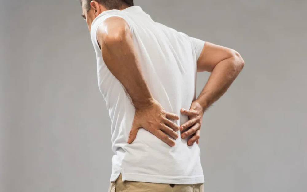 Mężczyzna w białej koszulce trzymający dłonie na dolnej części pleców, lekko pochylony do przodu