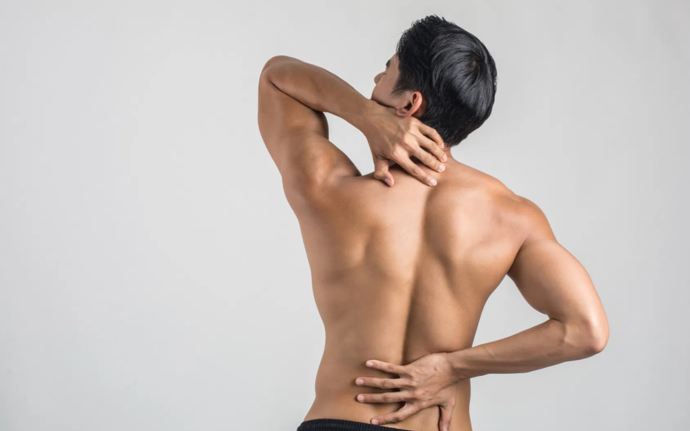 Osoba stojąca tyłem z odkrytymi plecami, jedną dłonią podtrzymująca dolny odcinek kręgosłupa, drugą sięgająca do górnej części pleców
