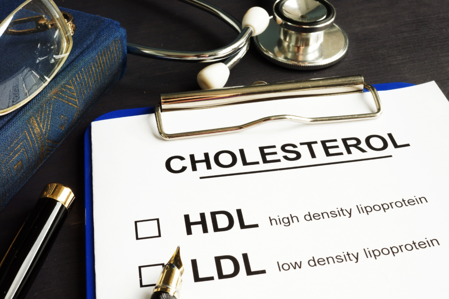 Dokument medyczny z napisem „Cholesterol” oraz oznaczeniami HDL i LDL, obok stetoskop i długopis, obraz przedstawiający diagnostykę poziomu cholesterolu i interpretację wyników badań.