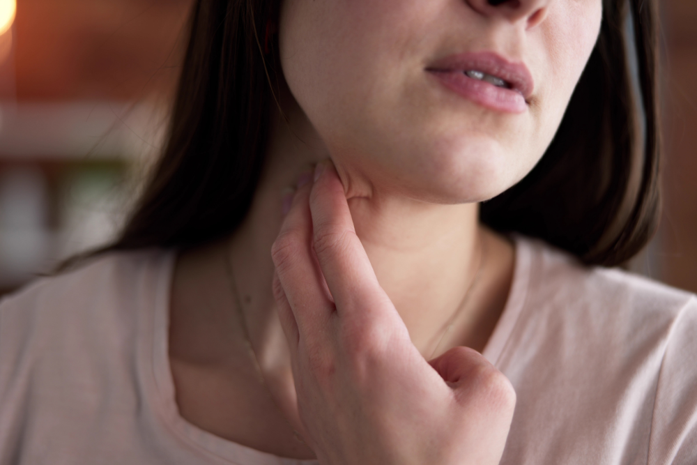 Osoba dotykająca palcami okolicy szyi i węzłów chłonnych, ujęcie górnej części klatki piersiowej i szyi