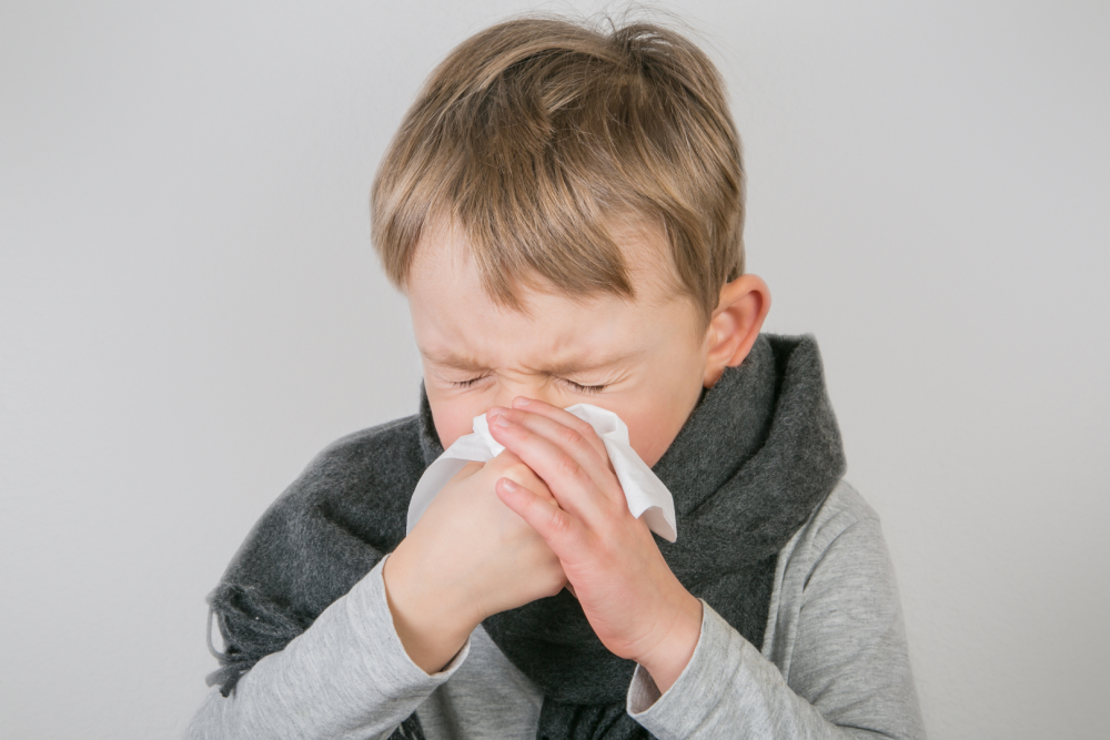 Dziecko ubrane w szary sweter i ciemny szalik, trzymające dłonie przy ustach