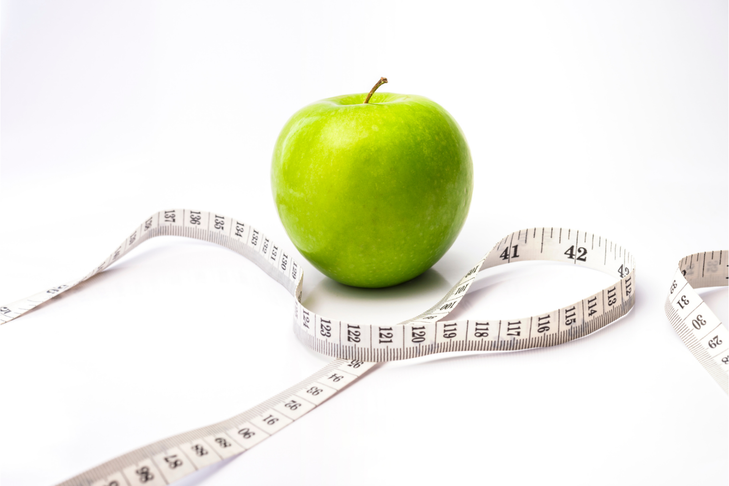 Zielone jabłko ułożone na białym tle, obok centymetr krawiecki zwinięty w pętlę