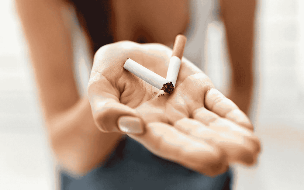 Dłoń trzymająca połamany papieros na jasnym tle