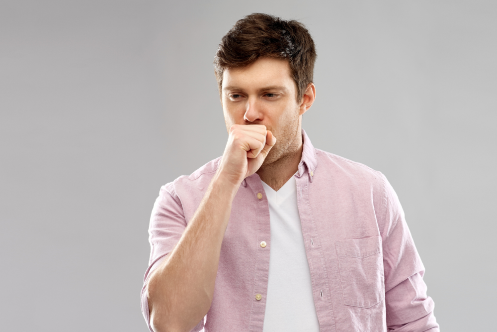 Mężczyzna w jasnoróżowej koszuli trzymający dłoń przy ustach