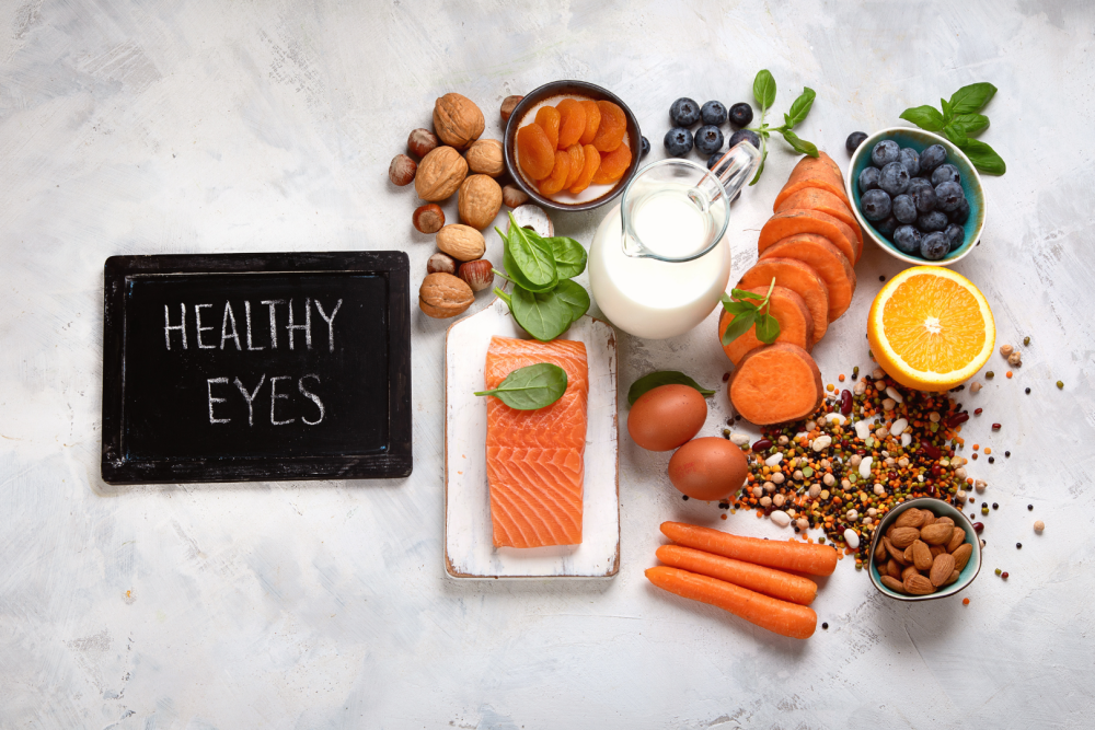 Kompozycja zdrowych produkt&oacute;w wspierających wzrok: łosoś, jajka, mleko, marchew, pomarańcza, bor&oacute;wki, orzechy i pestki, obok tabliczka z napisem Healthy Eyes