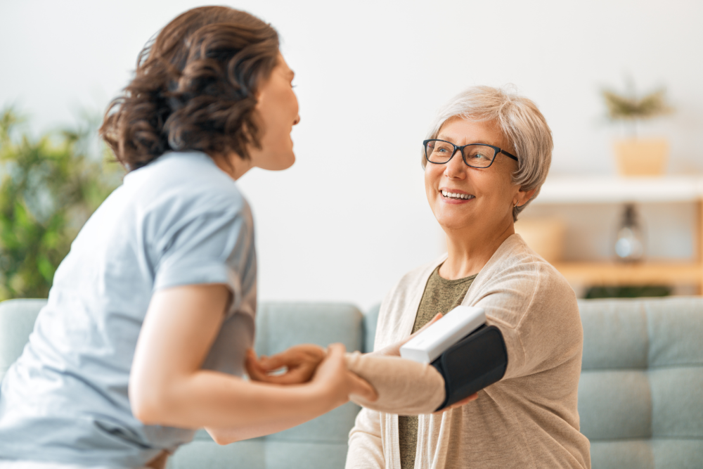 Opiekunka mierząca ciśnienie krwi starszej kobiecie w domowym wnętrzu, trzymająca jej ramię podczas badania