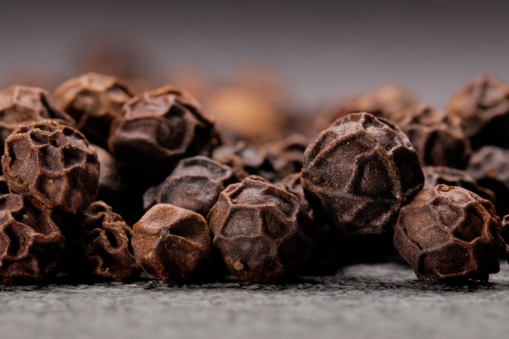 Zbliżenie na całe, suszone ziarna czarnego pieprzu o chropowatej strukturze, ułożone na ciemnym tle