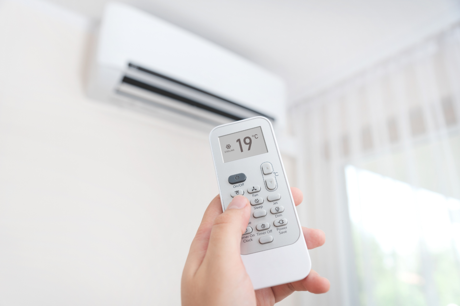 Pilot do klimatyzacji ustawionej na 19°C skierowany w stronę jednostki ściennej, obraz przedstawiający działanie klimatyzatora oraz wpływ niskiej temperatury nawiewu na komfort i zdrowie dróg oddechowych.