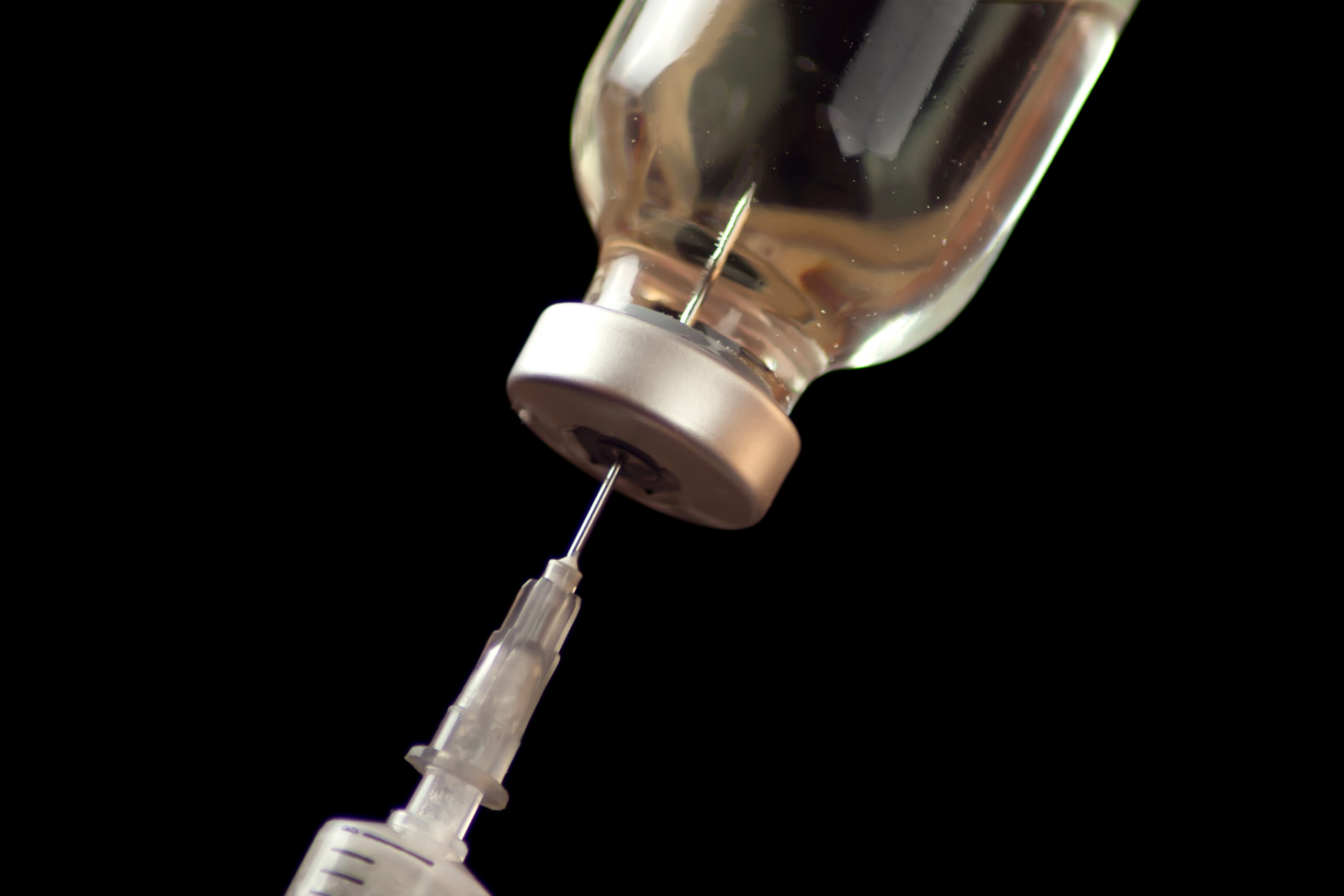 Fiolka z płynem połączona z igłą i strzykawką na czarnym tle