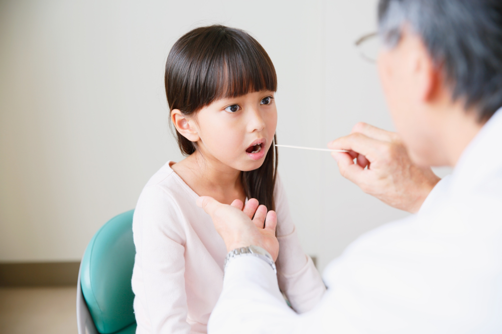 Lekarz w gabinecie bada gardło dziecka za pomocą patyczka diagnostycznego