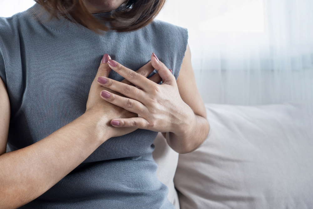 Osoba w szarej koszulce trzymająca obie dłonie na klatce piersiowej