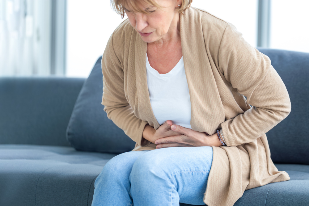 Osoba siedząca na kanapie w domowym wnętrzu, obejmująca brzuch obiema rękami