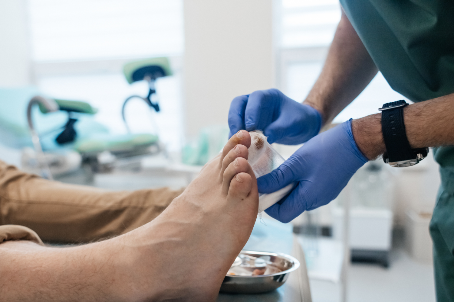 Zabieg medyczny polegający na opatrywaniu palców stopy przy użyciu jałowego bandaża, dłonie w jednorazowych rękawiczkach ochronnych, w tle gabinet zabiegowy