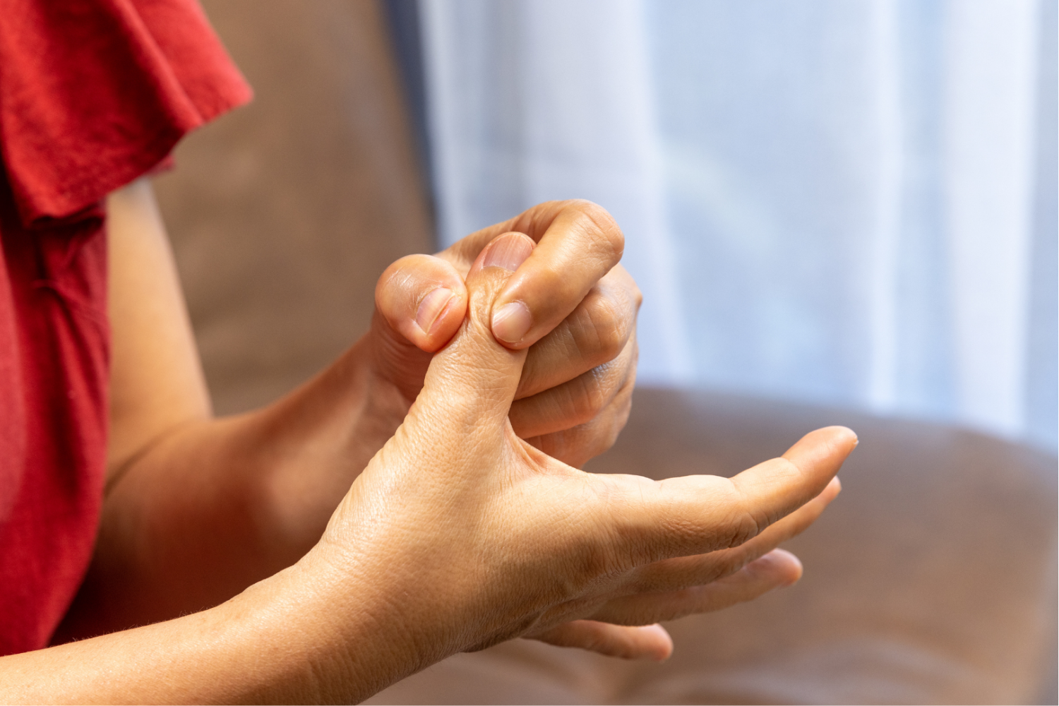 Zbliżenie na dłonie, jedna dłoń uciska palcem środkowym nasadę drugiego palca dłoni, tło neutralne