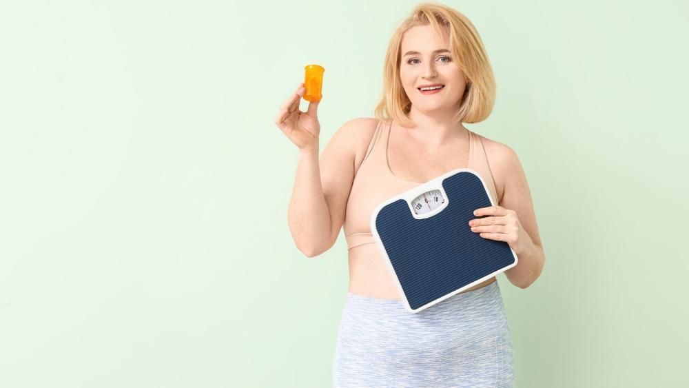 Kobieta trzymająca w jednej ręce wagę a w drugiej pojemnik z tabletkami