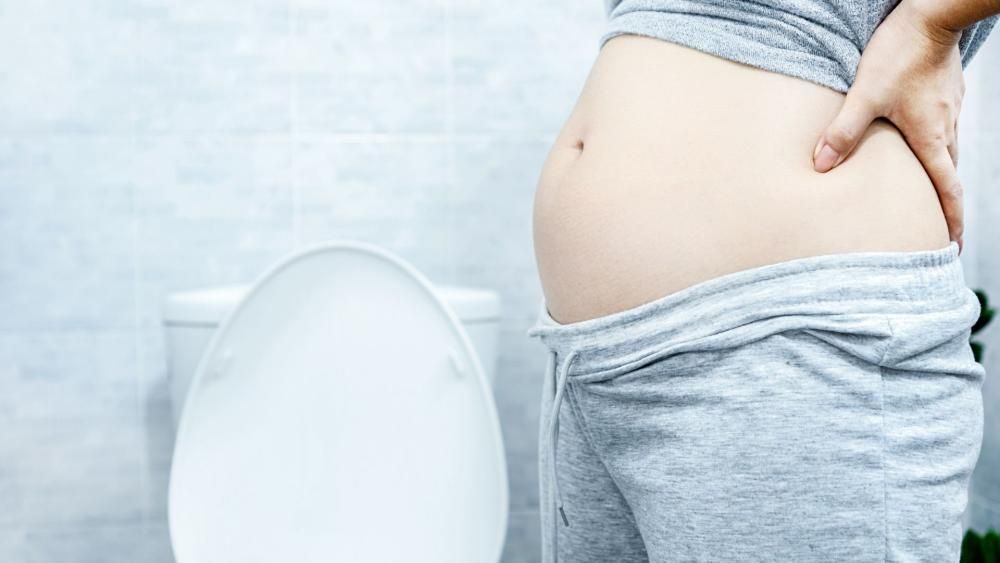 Wzdęty brzuch kobiety, która stoi przy klozecie