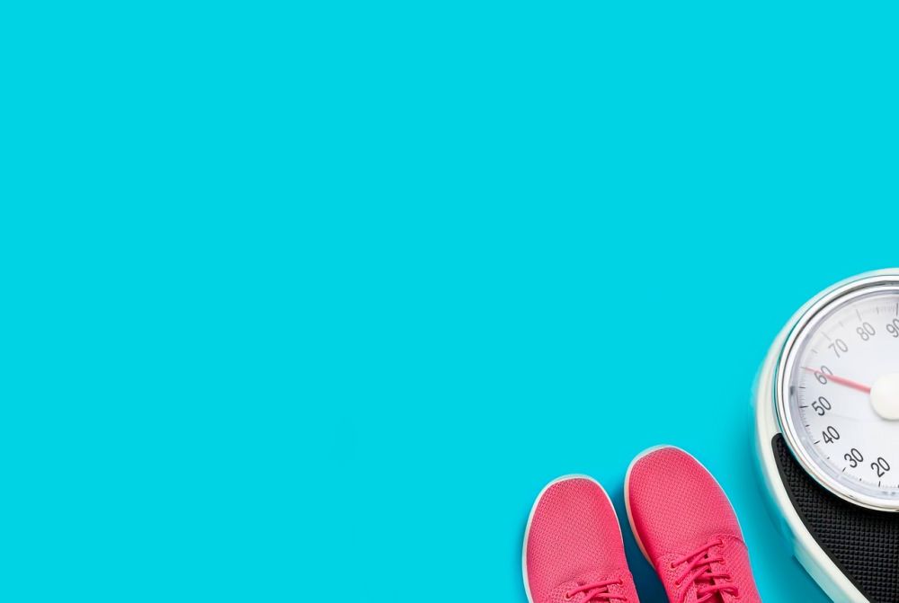 niebieskie tło a na nim waga oraz buty do biegania sportowe