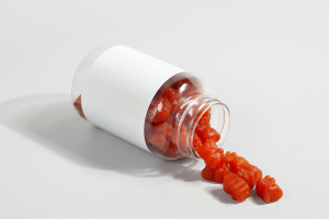 Przezroczysta butelka z białą etykietą, z której wysypują się czerwone żelki w kształcie niedźwiadków