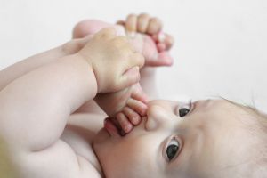 niemowle leży i wsadza sobie stopę do ust