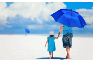 Dwie osoby idące po jasnej, piaszczystej powierzchni pod otwartym niebem, jedna osoba trzyma nad sobą niebieski parasol, druga osoba w jasnym stroju trzyma ją za rękę