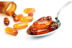 Przezroczyste kapsułki z bursztynową zawartością leżące na łyżce i wysypane z brązowej butelki na białym tle