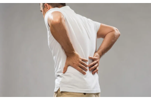 Mężczyzna w białej koszulce trzymający dłonie na dolnej części pleców, lekko pochylony do przodu
