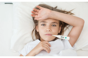 Dziecko leżące w łóżku z termometrem wskazującym 38,2°C, trzymające rękę na czole