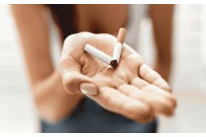 Dłoń trzymająca połamany papieros na jasnym tle