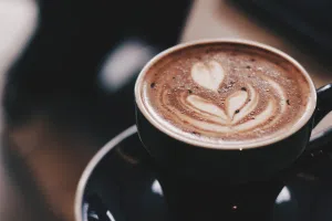 Filiżanka kawy z mleczną pianką i wzorem latte art w kształcie serca, obraz przedstawiający napój zawierający kofeinę, często analizowany pod kątem wpływu na ciśnienie tętnicze i zdrowie układu sercowo‑naczyniowego.