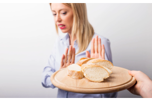 Dłoń podająca drewnianą deskę z kromkami białego pieczywa, osoba stojąca naprzeciwko unosi dłonie w geście odmowy