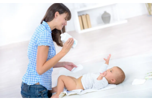 Rodzic zmieniający pieluchę niemowlęciu na przewijaku, trzymający w dłoni opakowanie chusteczek i pieluszkę