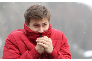 Osoba ubrana w czerwoną zimową kurtkę stojąca na zewnątrz podczas opadów śniegu, trzymająca dłonie blisko ust