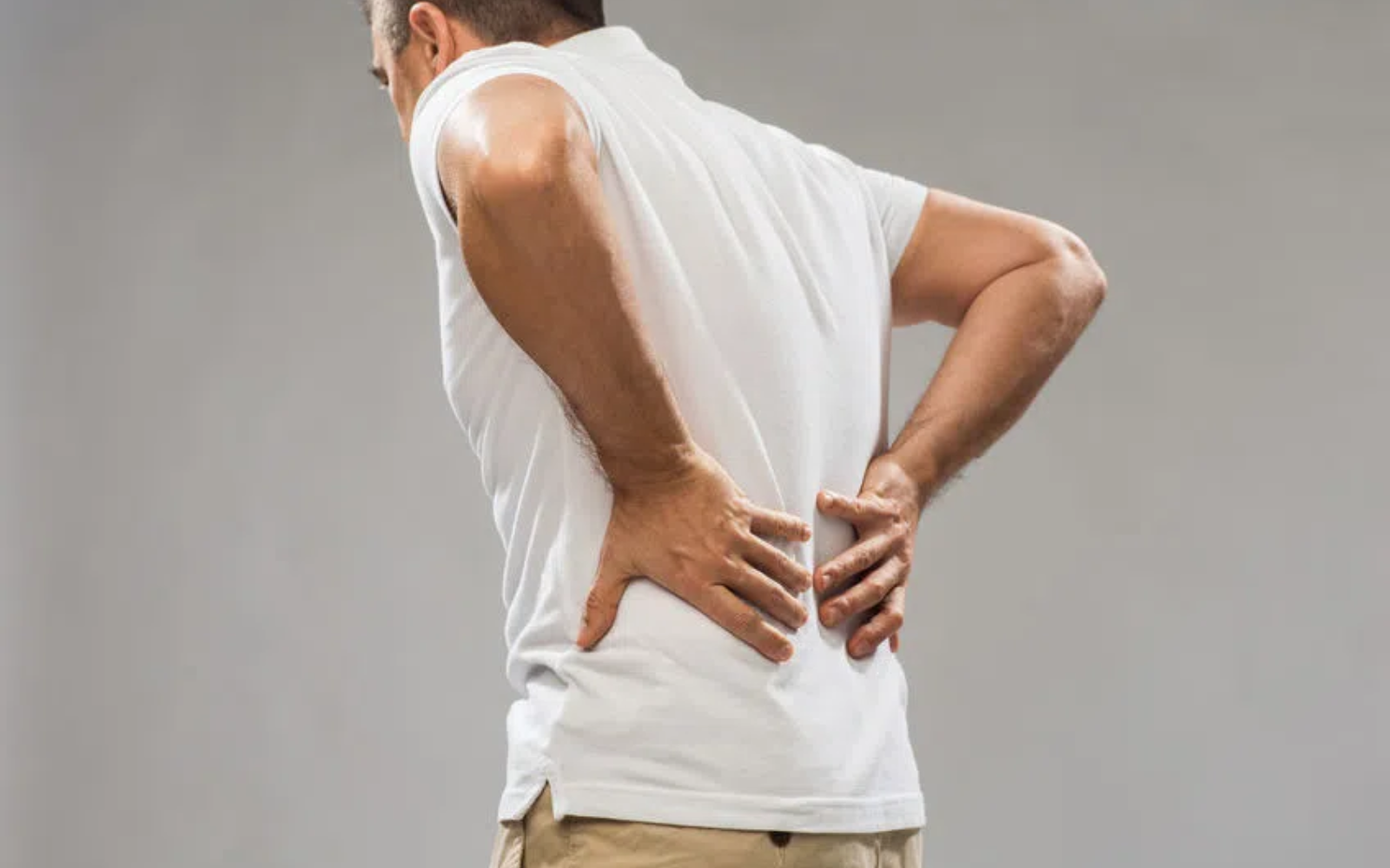 Mężczyzna w białej koszulce trzymający dłonie na dolnej części pleców, lekko pochylony do przodu
