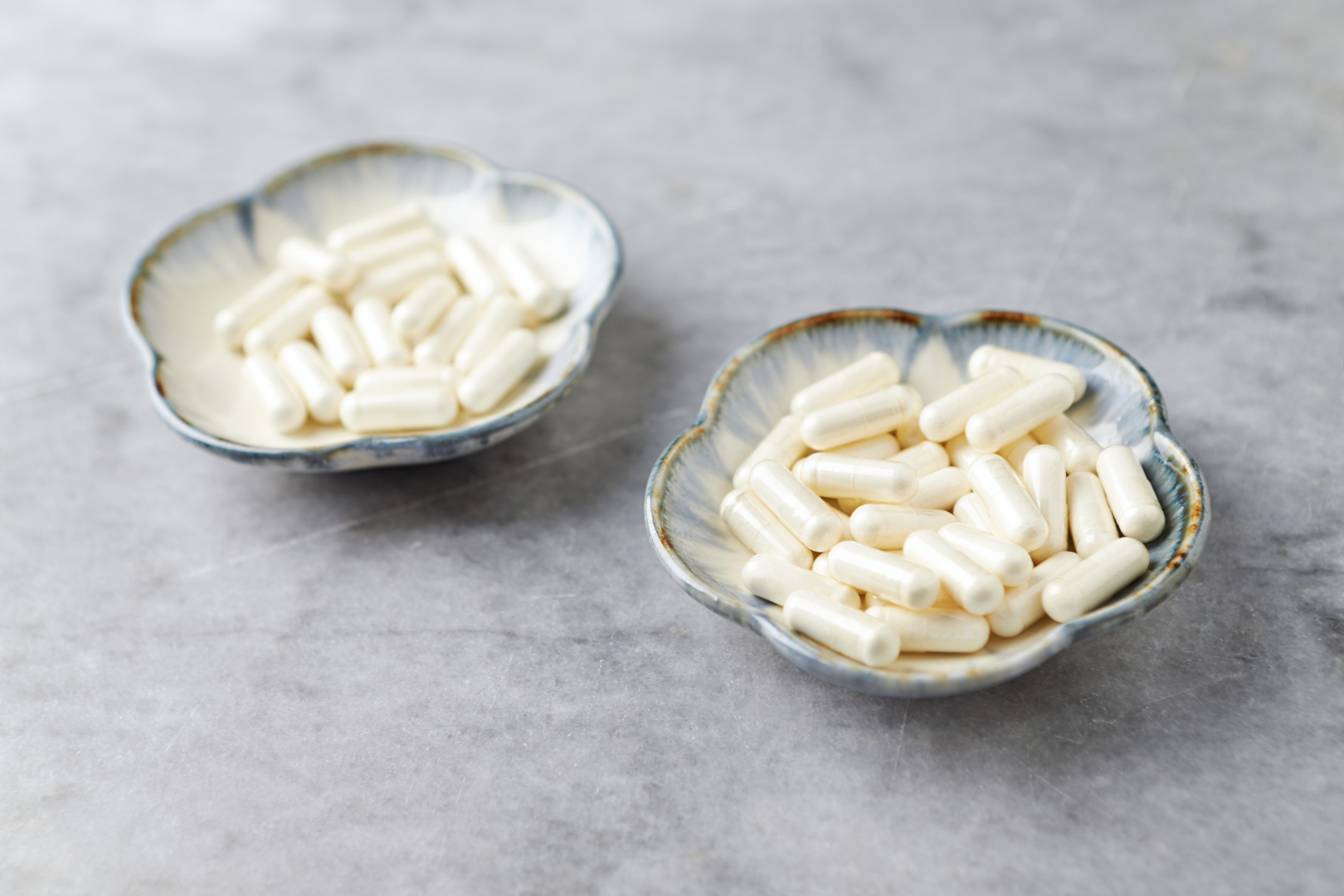 Dwie ceramiczne miseczki wypełnione białymi kapsułkami na jasnym kamiennym blacie