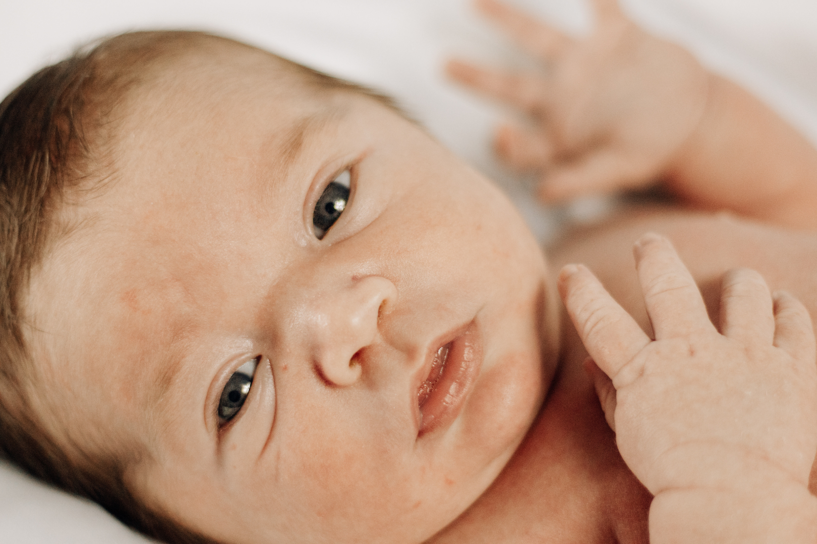 Niemowlę leżące na jasnym podłożu, z widoczną skórą torsu i dłońmi uniesionymi do góry