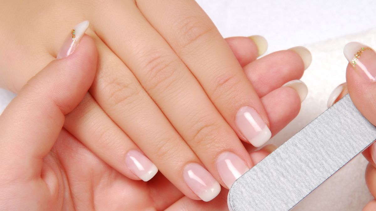 Zadbane naturalne paznokcie z klasycznym french manicure podczas domowego piłowania pilnikiem - podstawowy krok w pielęgnacji paznokci podczas ich zapuszczania.